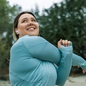 Mulher adulta sorrindo e se alongando no parque, fazendo exercícios para prevenir a sarcopenia.