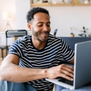 Jovem adulto feliz usando o laptop enquanto descansa no sofá em casa.