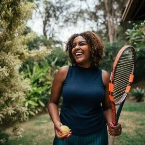 Mulher sorrindo com raquete e bola de tênis, representando energia e vitalidade.