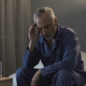 Homem insone sofrendo de dor de cabeça, sentado no sofá à noite.