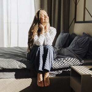 Mulher sentada na cama, sorrindo e se espreguiçando depois de acordar.