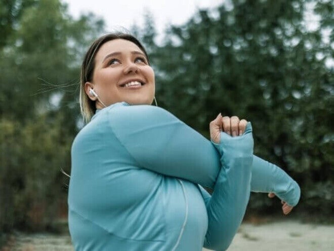 Mulher adulta sorrindo e se alongando no parque, fazendo exercícios para prevenir a sarcopenia.