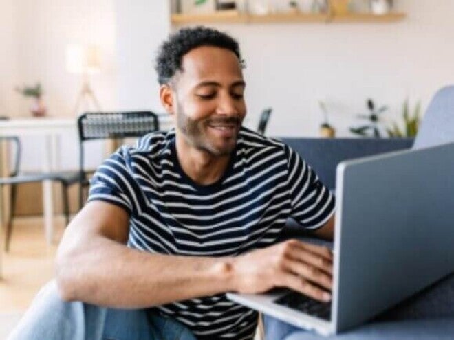 Jovem adulto feliz usando o laptop enquanto descansa no sofá em casa.