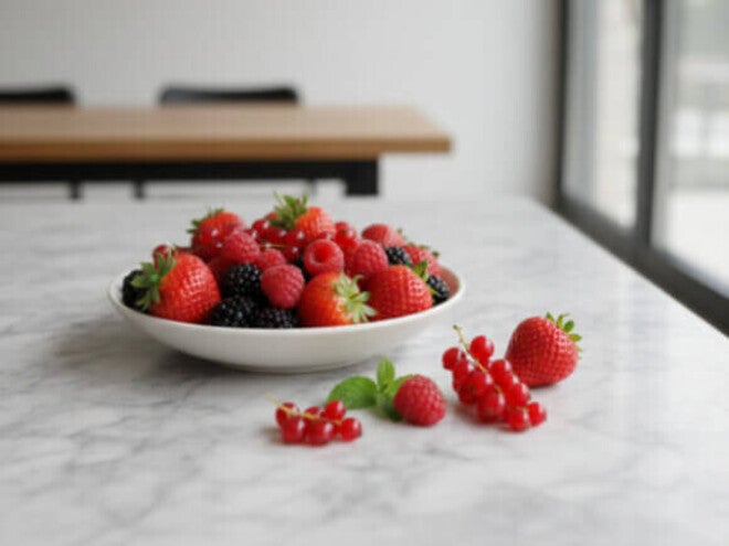 Tigela branca cheia de morangos, framboesas e amoras em uma bancada de mármore branco, frutas ricas em colágeno. 