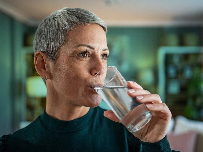 Mulher adulta bebendo um copo de água.