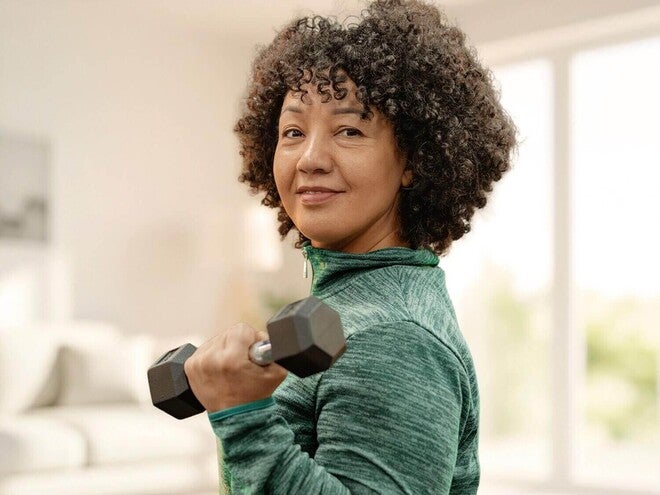 Mulher adulta fazendo treino de força com pesos na sala de casa.
