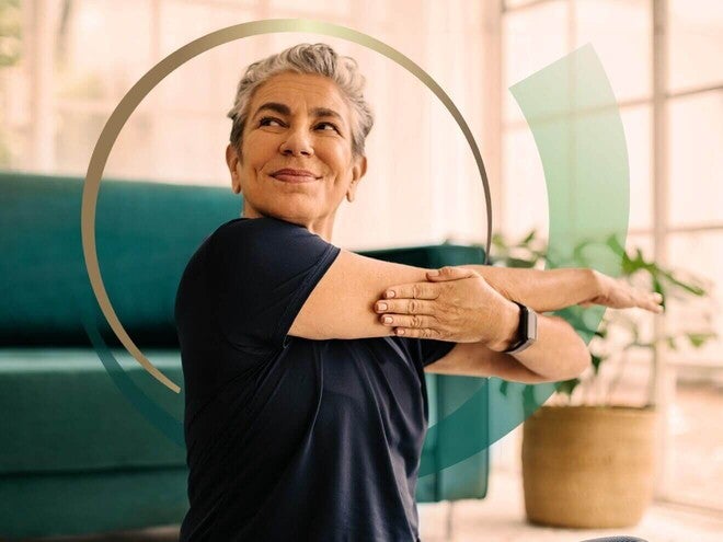 Mulher mais velha fazendo um alongamento suave na sala de casa.