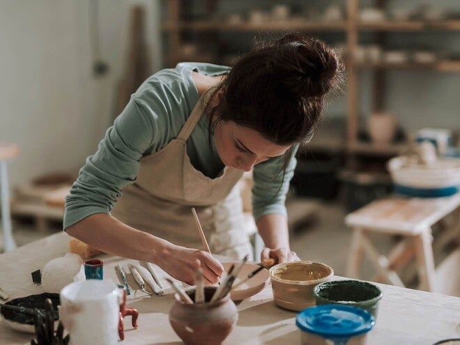Mulher pintando uma peça de cerâmica com um pincel em um ateliê, usando um avental.
