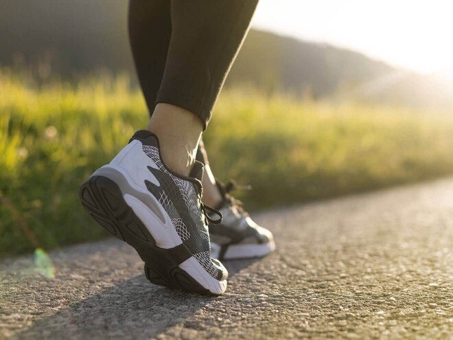Close-up de pés caminhando em um caminho de asfalto ao ar livre, com luz de amanhecer, representando caminhada diária para a saúde