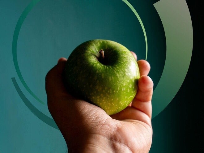 Mão adulta segurando uma maçã verde.