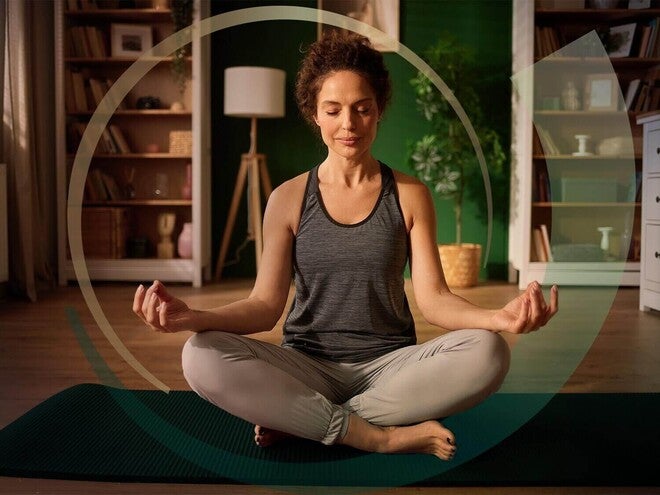 Pessoa em posição de yoga de pernas cruzadas, sentada em um carpete, relaxada e feliz.