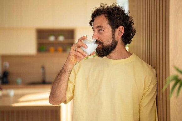 Homem adulto bebendo um copo de Nestlé Vital Ritual Noturno. Suplemento de colágeno.