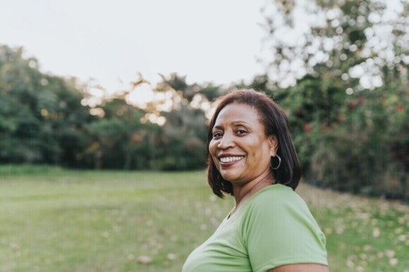 Mulher feliz sorrindo em um parque recebendo vitamina D3 do sol