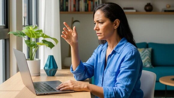 Mulher brasileira adulta com mais de 35 anos concentrada, olhando para um laptop, em um home office iluminado.